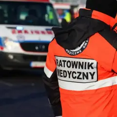 Ratownik medyczny w pomarańczowej kurtce stoi obok karetki pogotowia.
