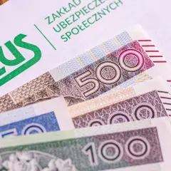 ZUS na białej kopercie, pod nią polskie banknoty 500, 200 i 100 zł. Czekamy na 14. emeryturę.