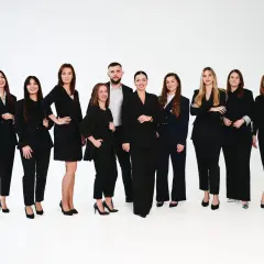 Grupa profesjonalistów w czarnych garniturach pozuje na białym tle.