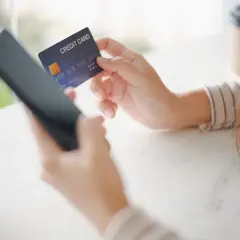 Kobieta trzyma kartę kredytową i telefon, przygotowując się do płatności online. Może to być początek procesu, który w razie problemów zakończy się chargeback.