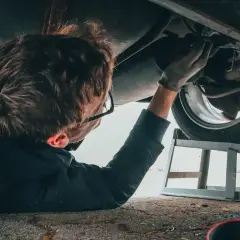 Mechanik pod samochodem, zastanawia się ile zarabia diagnosta samochodowy.