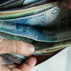 Ręka przegląda portfel pełen polskich banknotów. Widać wyraźnie banknot 100 zł, a także 50 zł i inne nominały.