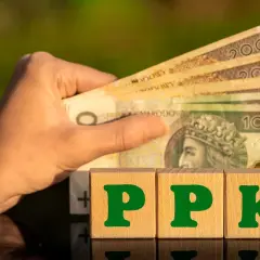 Dłoń trzyma polskie banknoty. Obok kostki z literami PPK. Co to PPK? To przyszłość Twoich oszczędności.