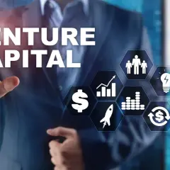 Biznesmen wskazuje na ekran z napisem VENTURE CAPITAL i ikonami symbolizującymi rozwój, pieniądze i innowacje.