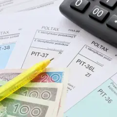 Formularze podatkowe PIT, polskie banknoty, żółty długopis i kalkulator.