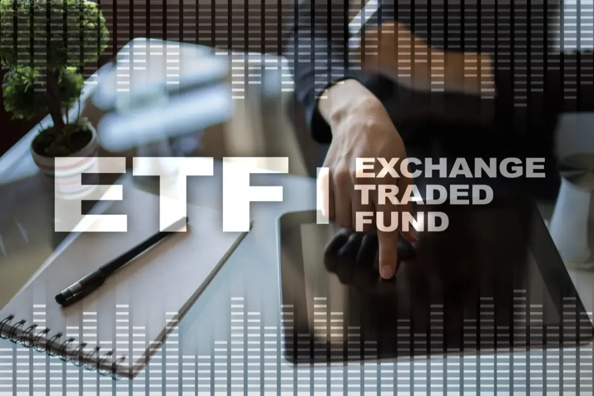 Ręka dotyka ekranu tabletu z napisem ETF (Exchange Traded Fund) na tle wykresów.