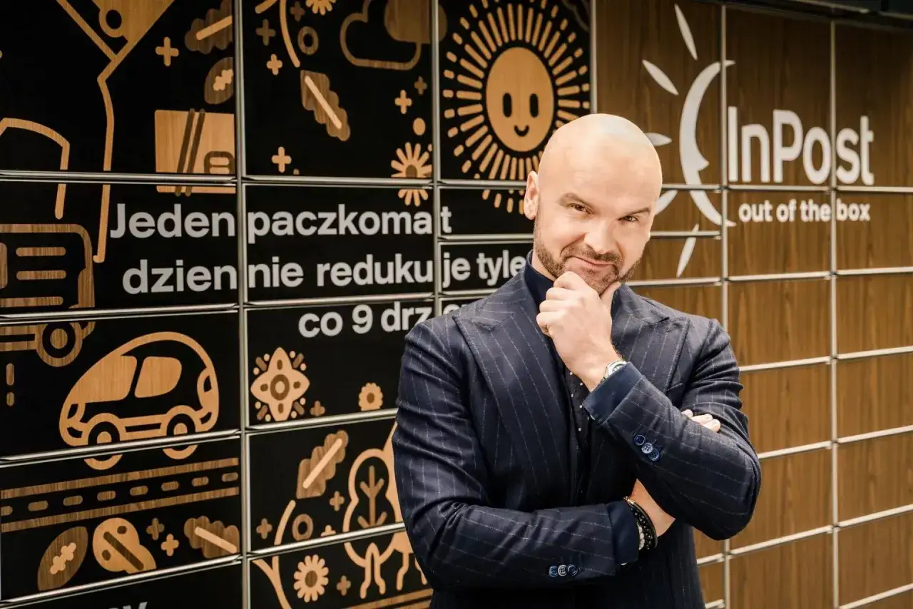 Rafał Brzoska, twórca InPost, zamyślony na tle paczkomatów. Jego majątek to symbol sukcesu.