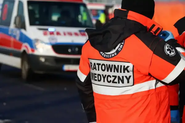 Ratownik medyczny w pomarańczowej kurtce stoi obok karetki pogotowia.
