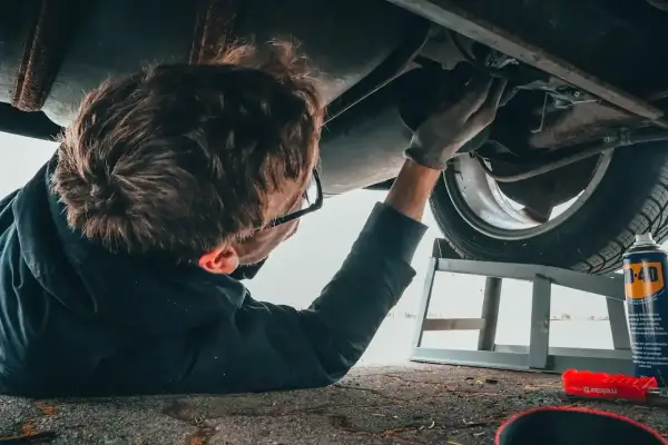 Mechanik pod samochodem, zastanawia się ile zarabia diagnosta samochodowy.