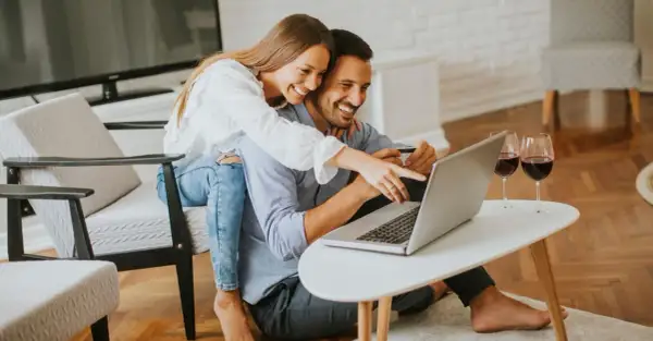 Szczęśliwa para robi zakupy online, ciesząc się ulgą na internet i lampką wina.