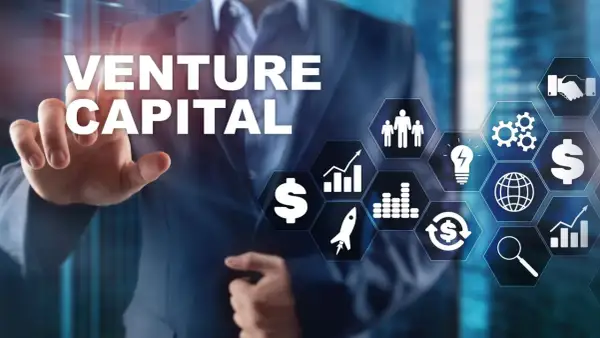 Biznesmen wskazuje na ekran z napisem VENTURE CAPITAL i ikonami symbolizującymi rozwój, pieniądze i innowacje.