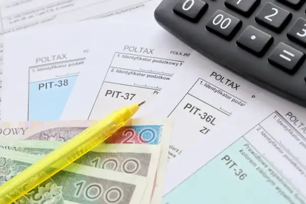 Formularze podatkowe PIT, polskie banknoty, żółty długopis i kalkulator.