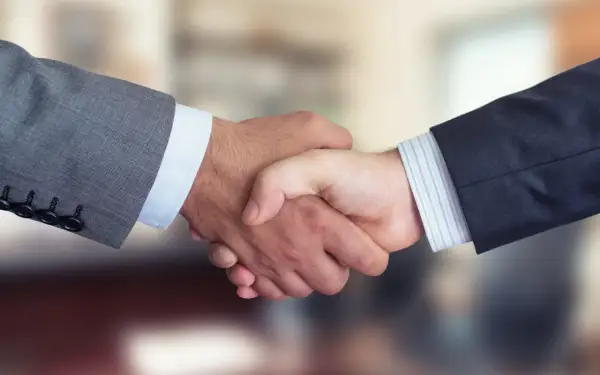 Dwaj mężczyźni w garniturach ściskają sobie dłonie, symbolizując udane joint venture i partnerstwo biznesowe.